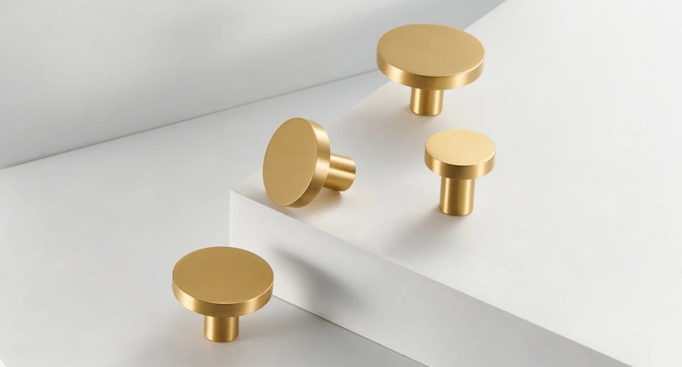 Four gold brass round cabinet knobs on a white geometric background.