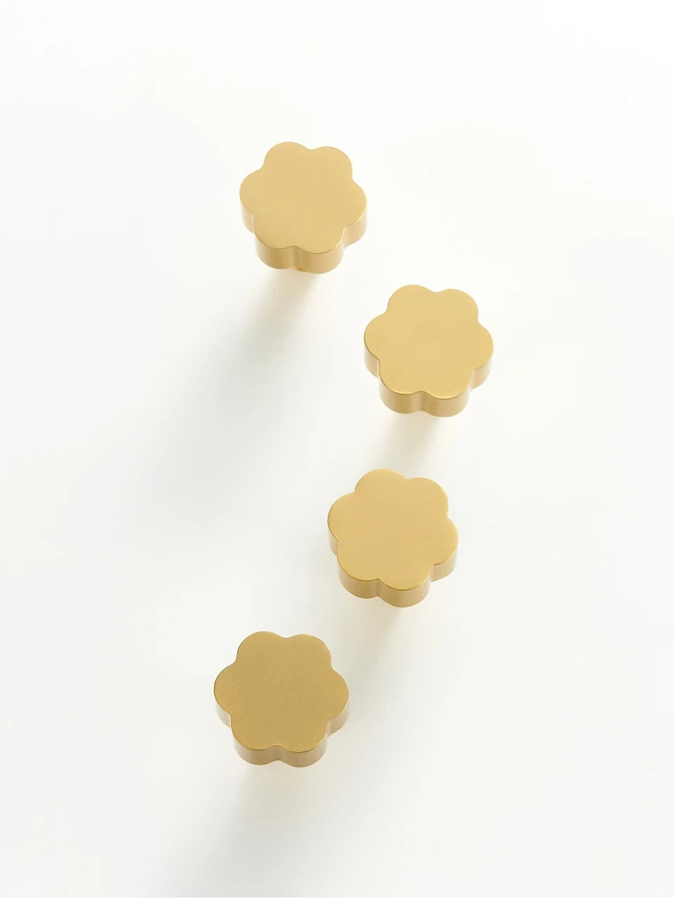 Four gold flower cabinet knobs on a white background.