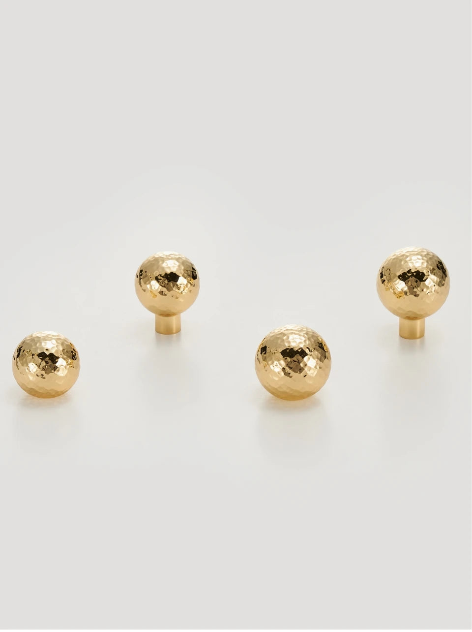 Set of four gold hammered knobs on a white background.