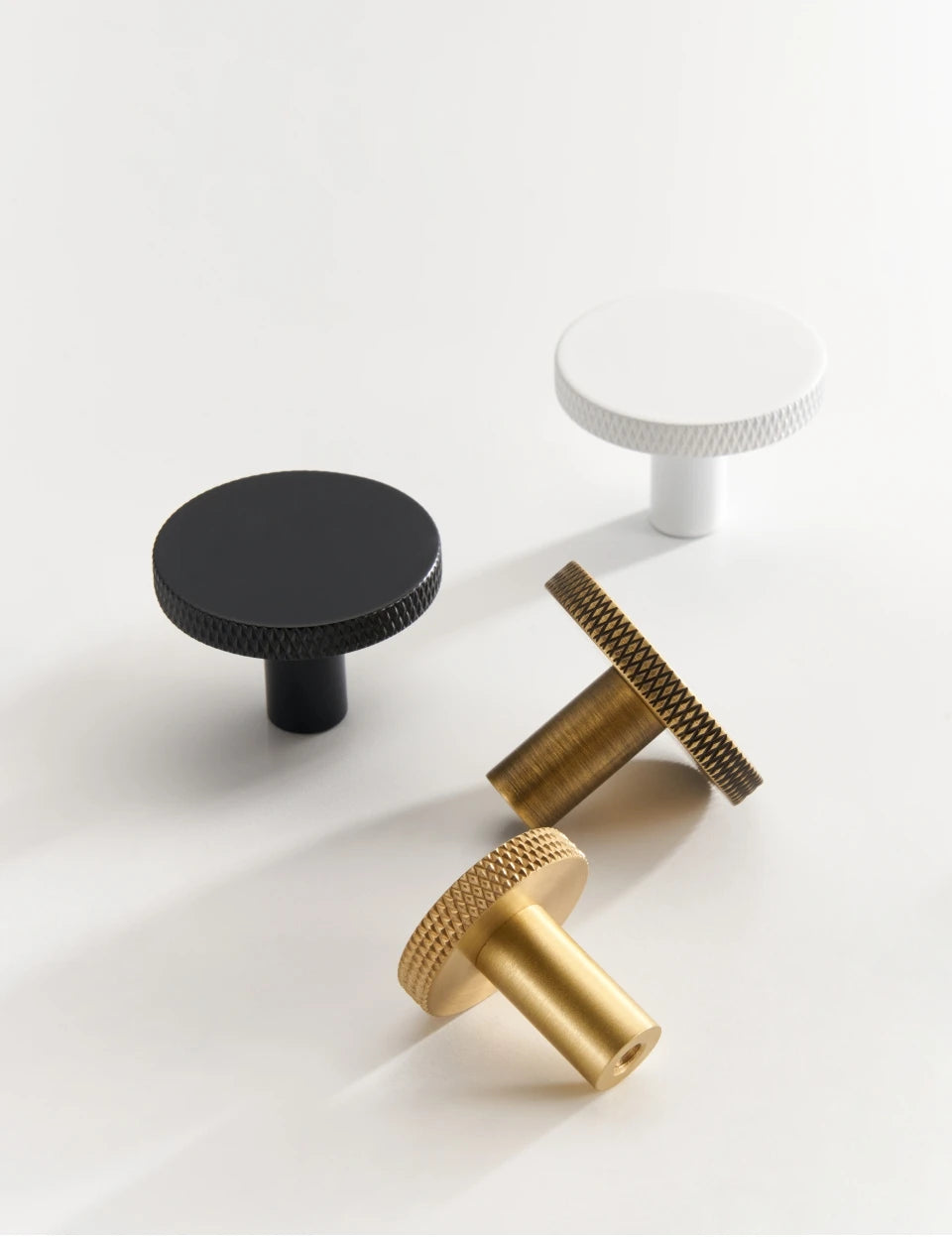 Four matte antique cabinet knobs in black, gold, antique brass and white on a white background.