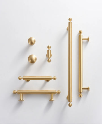 Collection of French luxury brass gold cabinet handles knobs and t-bar on a light gray background