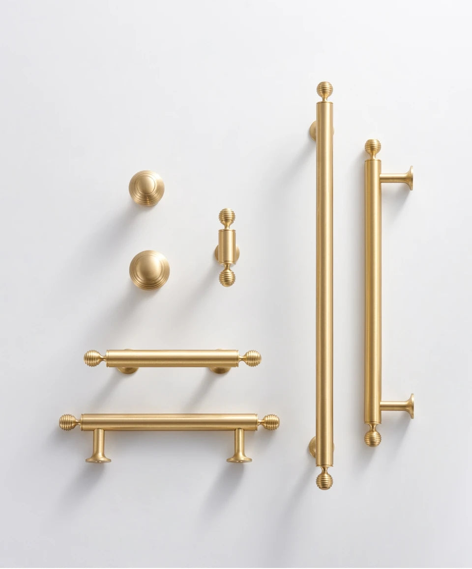 Collection of French luxury brass gold cabinet handles knobs and t-bar on a light gray background