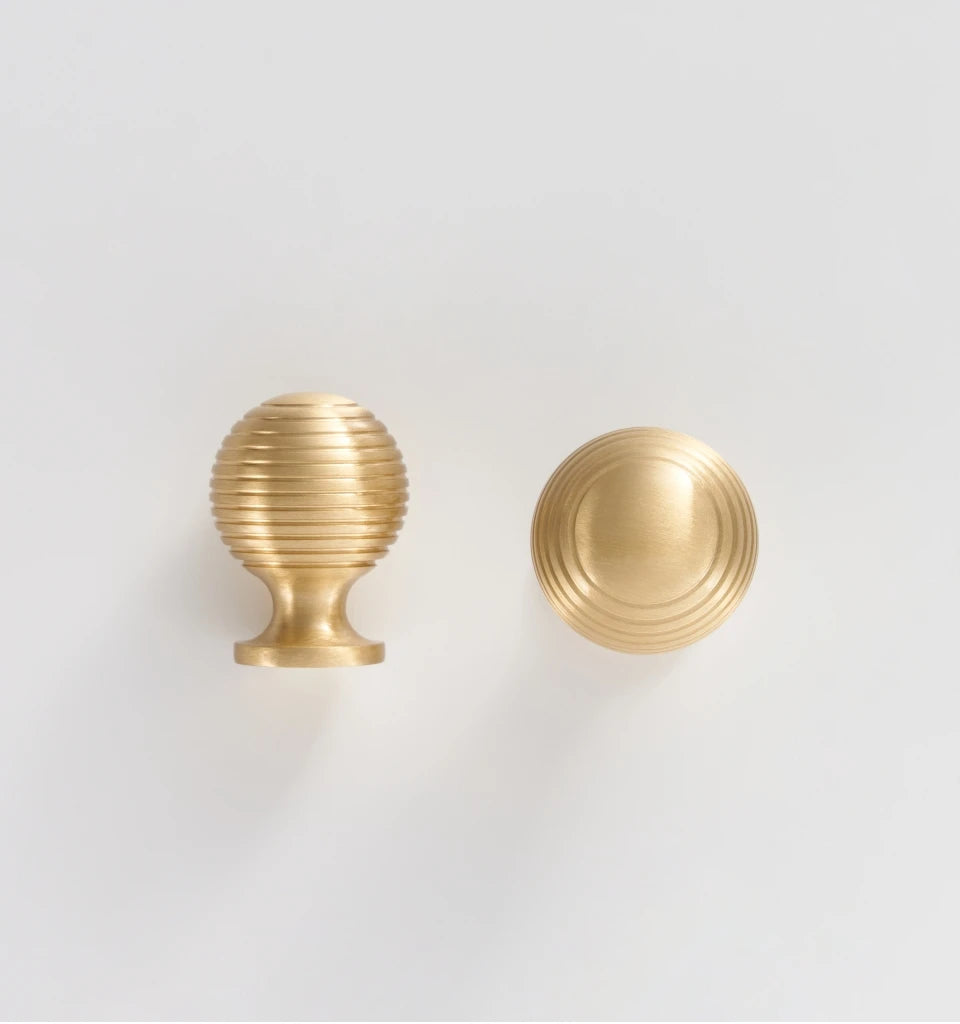 Two French luxury brass gold door knobs on a beige surface with a white background.
