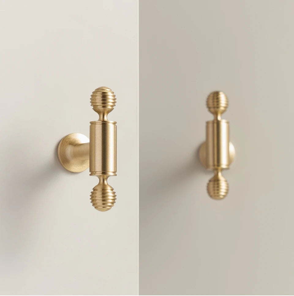 Pair of French luxury brass gold t-bars on a beige surface.