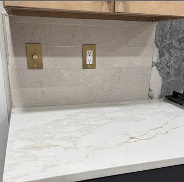 Marble-patterned kitchen countertop with gold fixtures and dark cabinets.