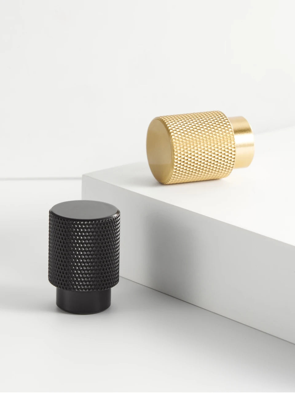 Three knurled brass knobs in black, gold, and bronze on a light grey background.
