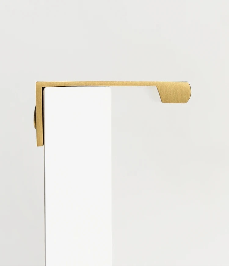 Gold brass edge pull on a white cupboard door from side.