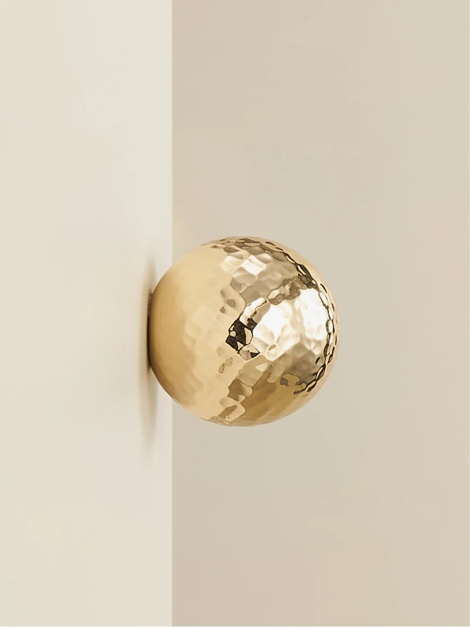 Gold brass hammered cabinet knob on a white door.