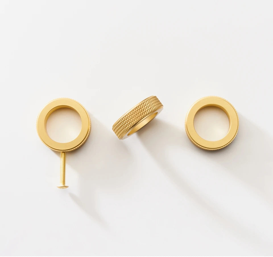 Gold knurled brass ring cabinet knobs with a screw on a white background.