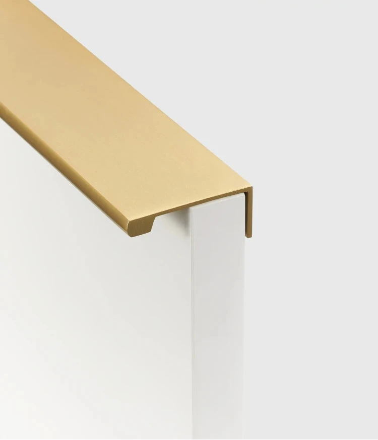 Gold cabinet edge pull on a beige cupboard door from the side.