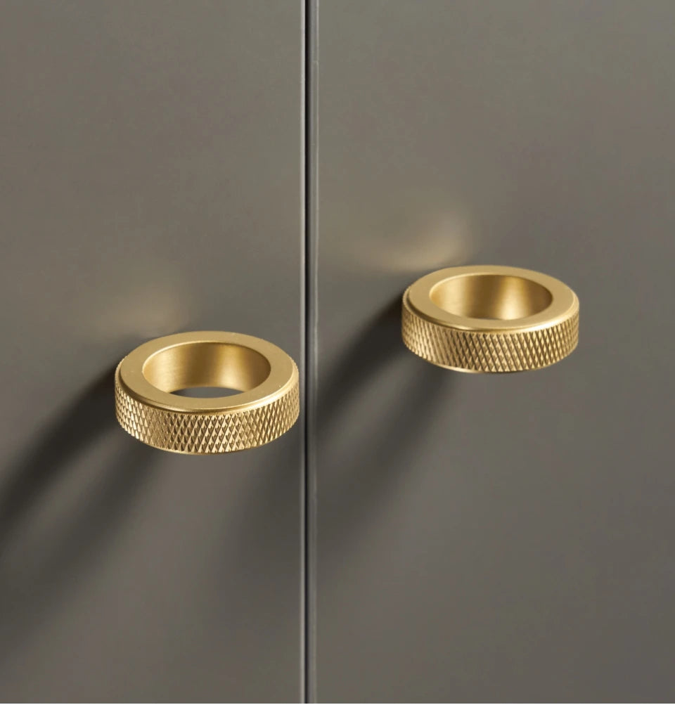 Two gold knurled brass ring cabinet knobs on a grey cabinet.