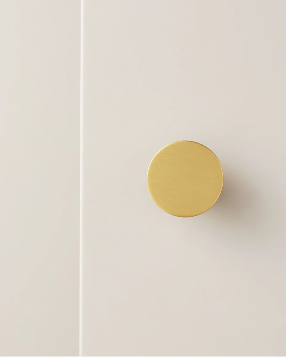 One gold brass round knob on a white cabinet door.