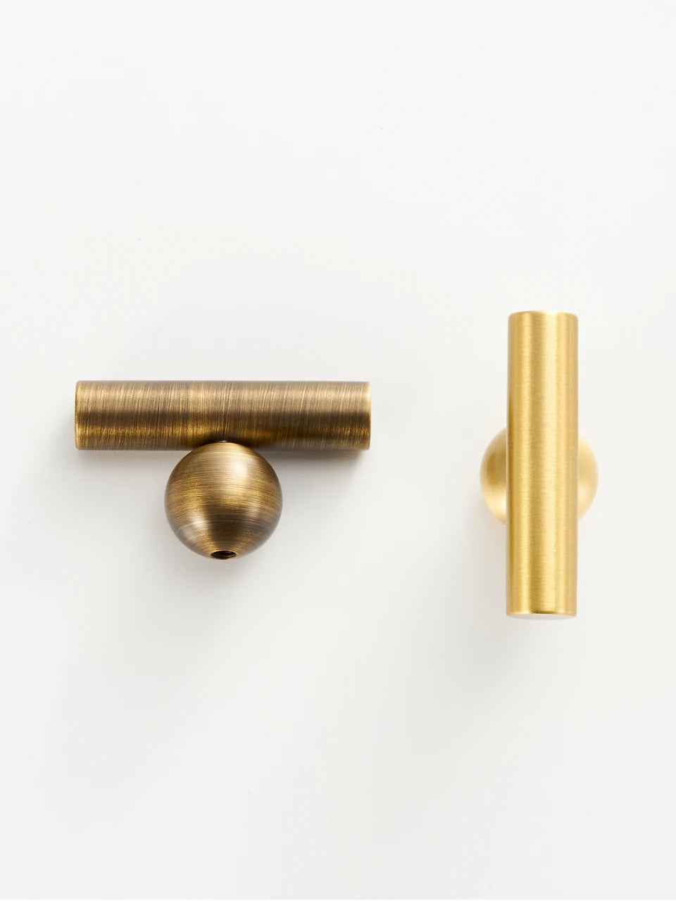 Pair of gold and antique brass round ball t-bars on a white surface.