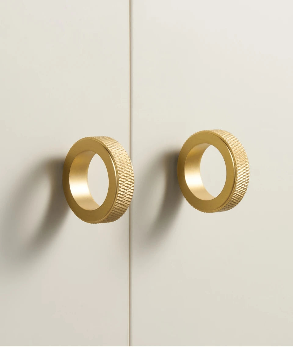 Pair of gold knurled ring cabinet knobs on a light beige background.