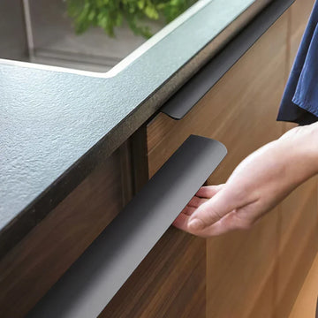 Person using a kitchen cabinet edge pull with a sink and countertop in the background.