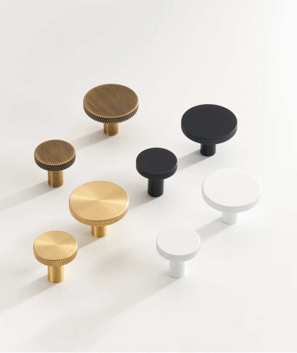 Set of gold, black, antique brass and white  matte antique cabinet knobs on a white background.