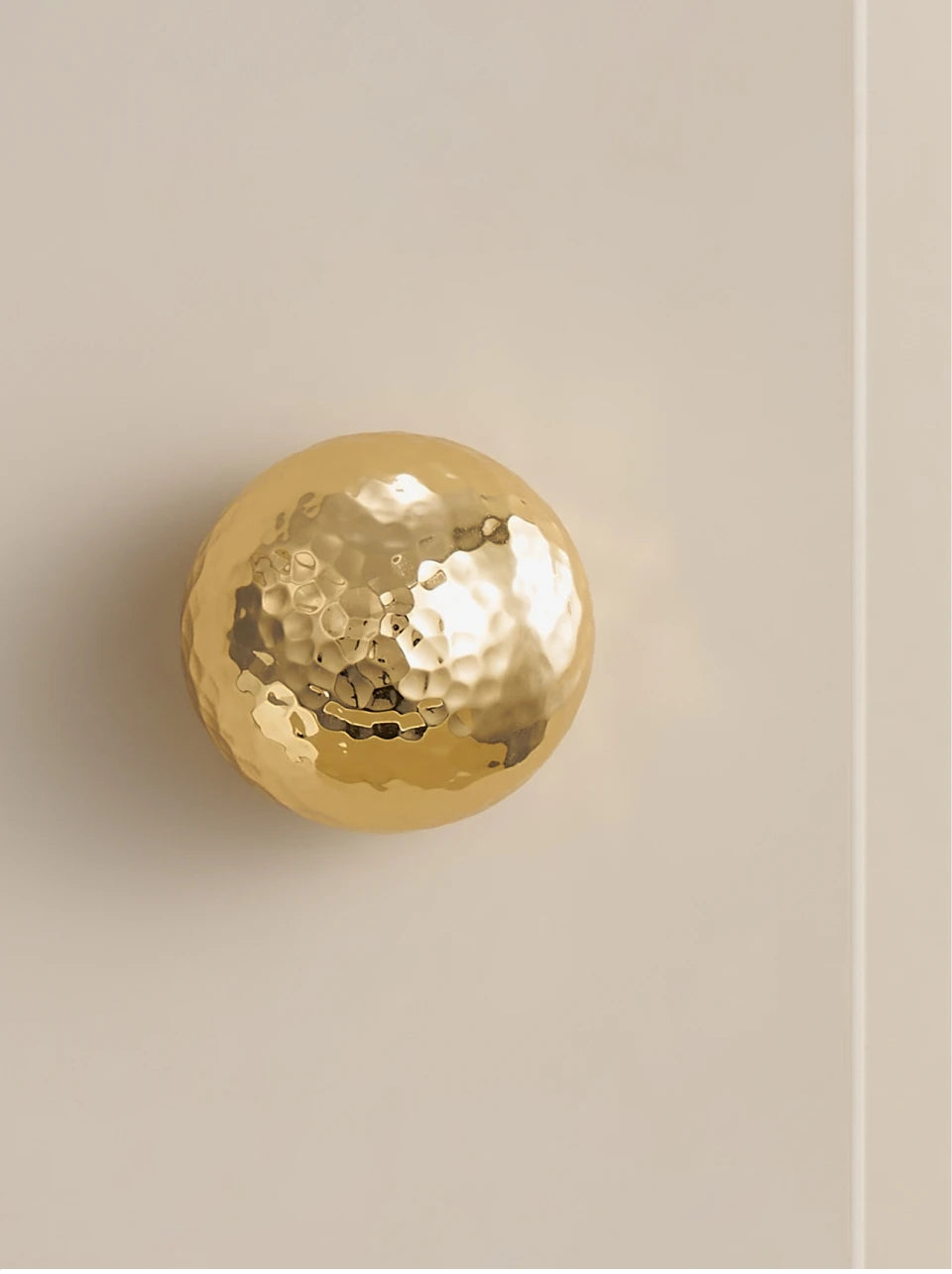 Single gold hammered brass knob on a beige cabinet door.