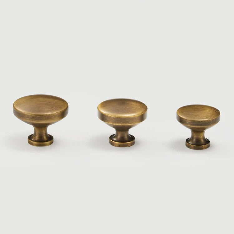 Three antique brass cabinet knobs on a white background.