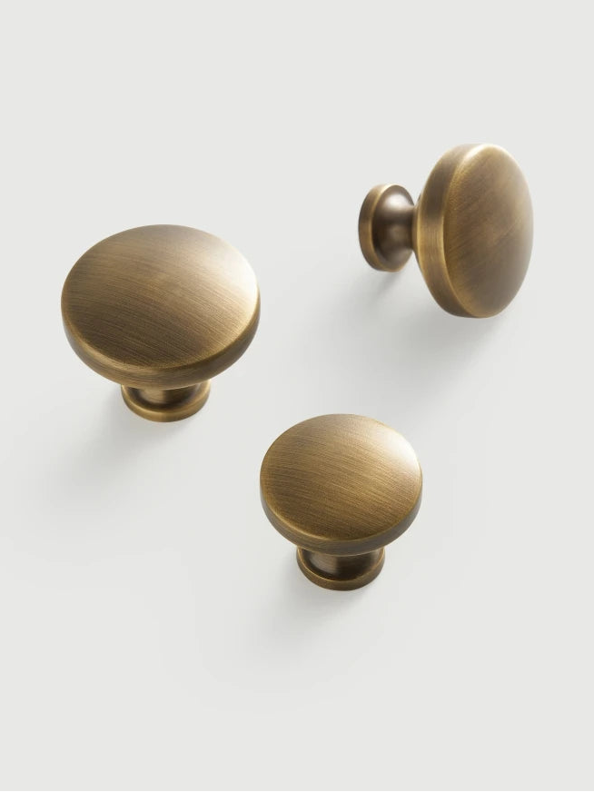 Three brass cabinet knobs on a neutral background .
