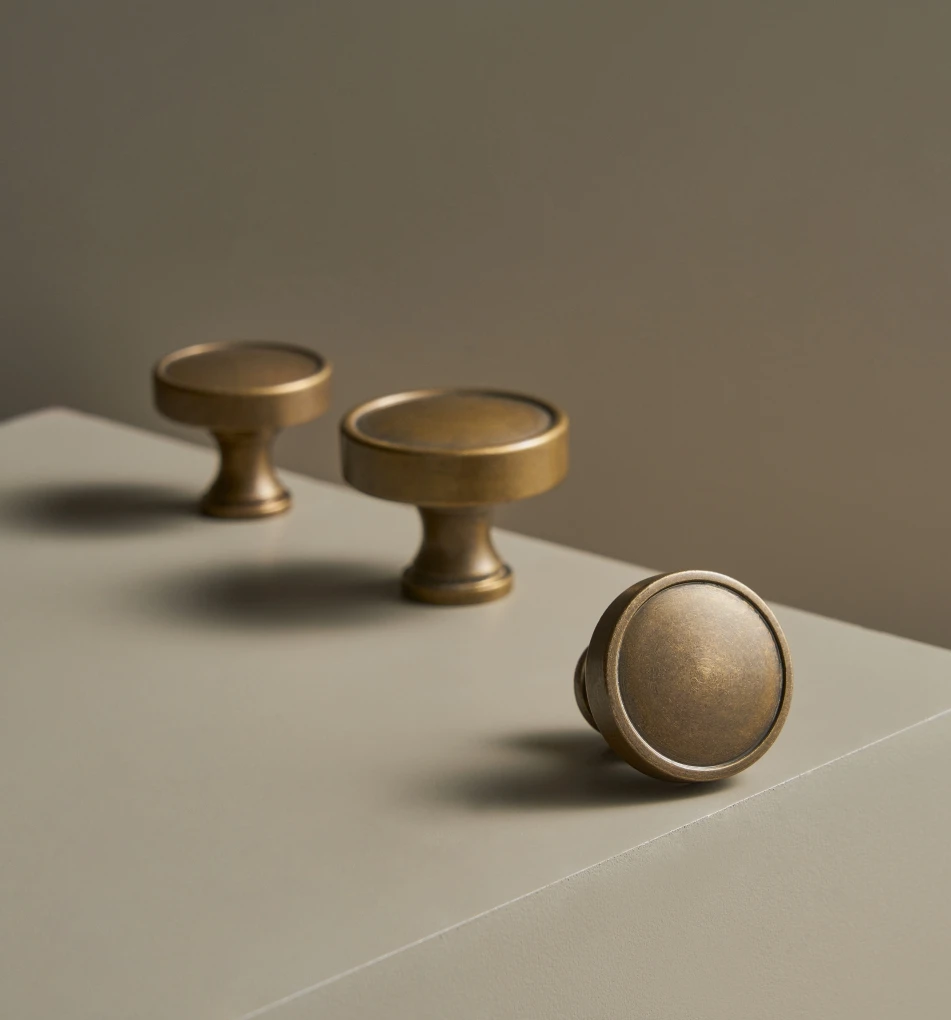 Three brass countryside style cabinet knobs on a neutral background.