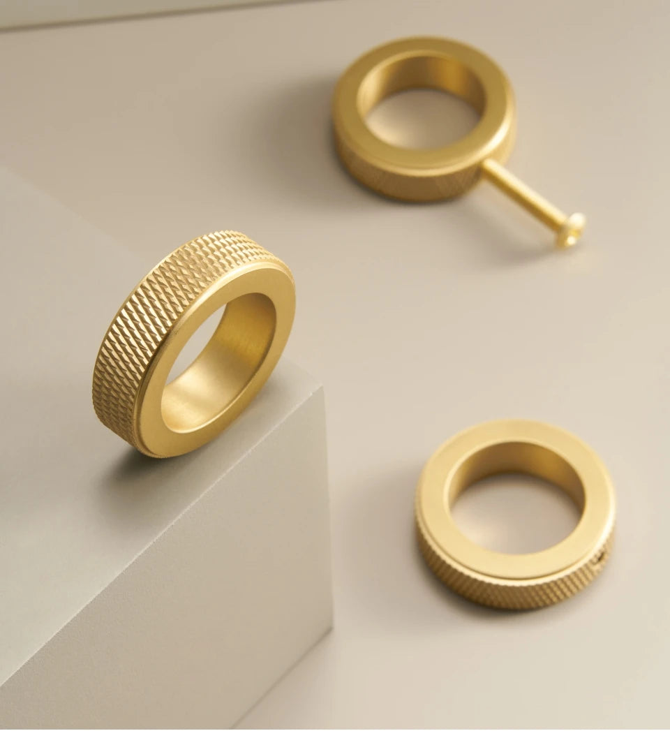 Three gold knurled ring cabinet knobs on a light beige background.