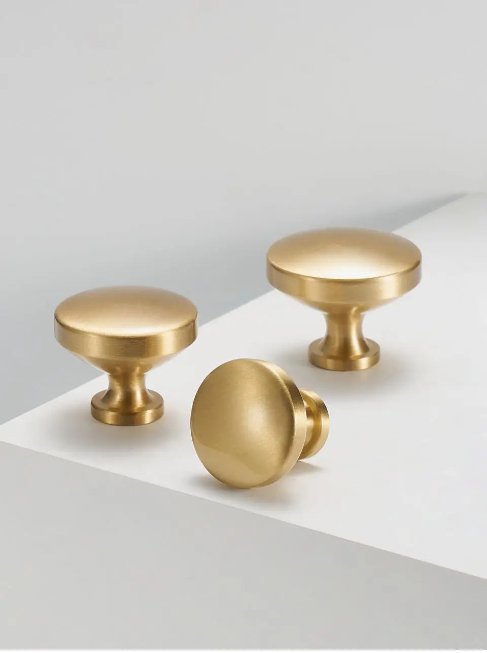 Three gold solid brass cabinet knobs on a white surface with a light grey background.