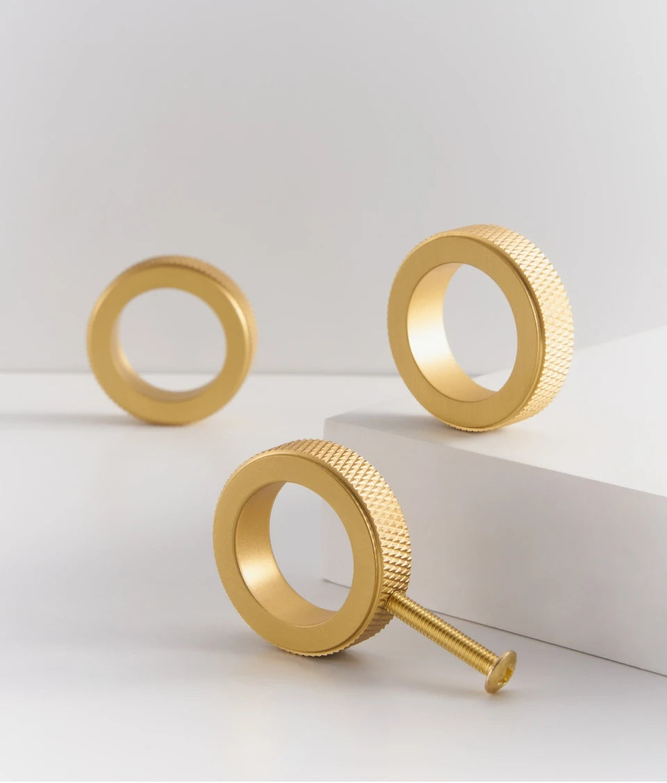 Three gold knurled brass ring cabinet knobs with a central ring featuring a screw on a white background.