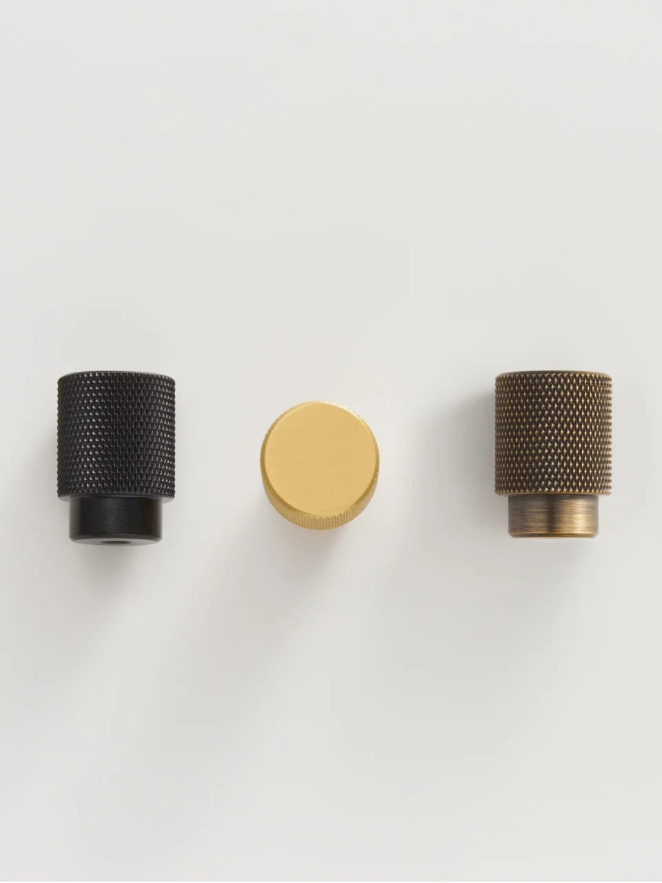 Three knurled brass knobs in black, gold, and bronze on a light grey background.