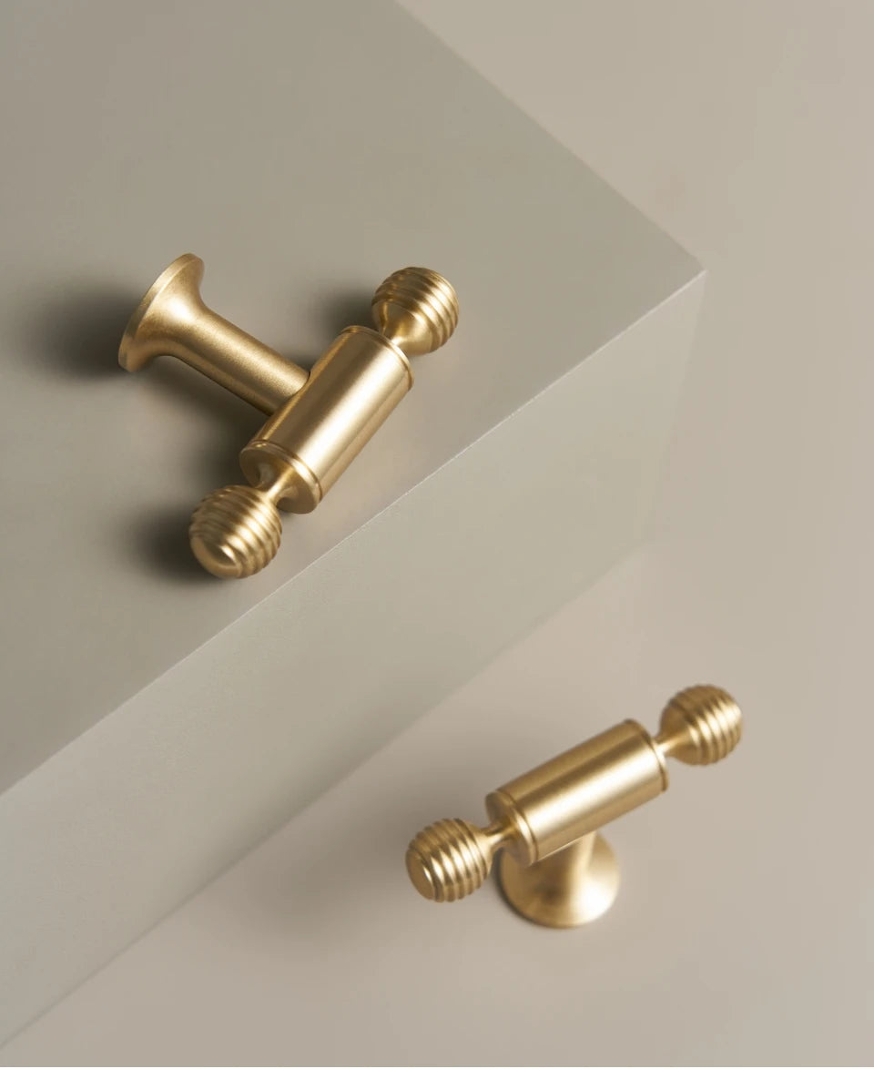Two French luxury brass gold t-bars on a beige surface with a beige background.