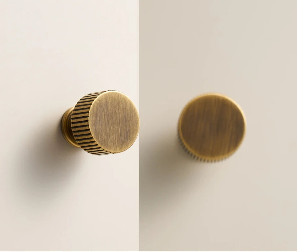 Two antique brass Art Deco cabinet knobs on a light beige background.