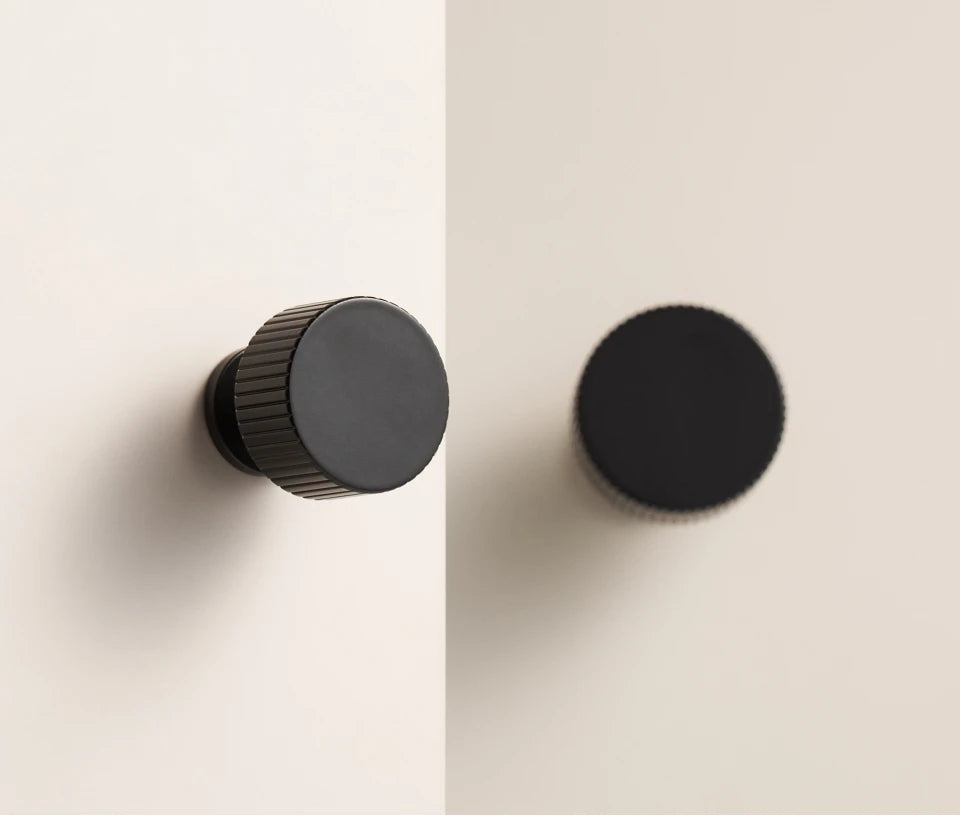Two black art deco cabinet knobs on a beige background.