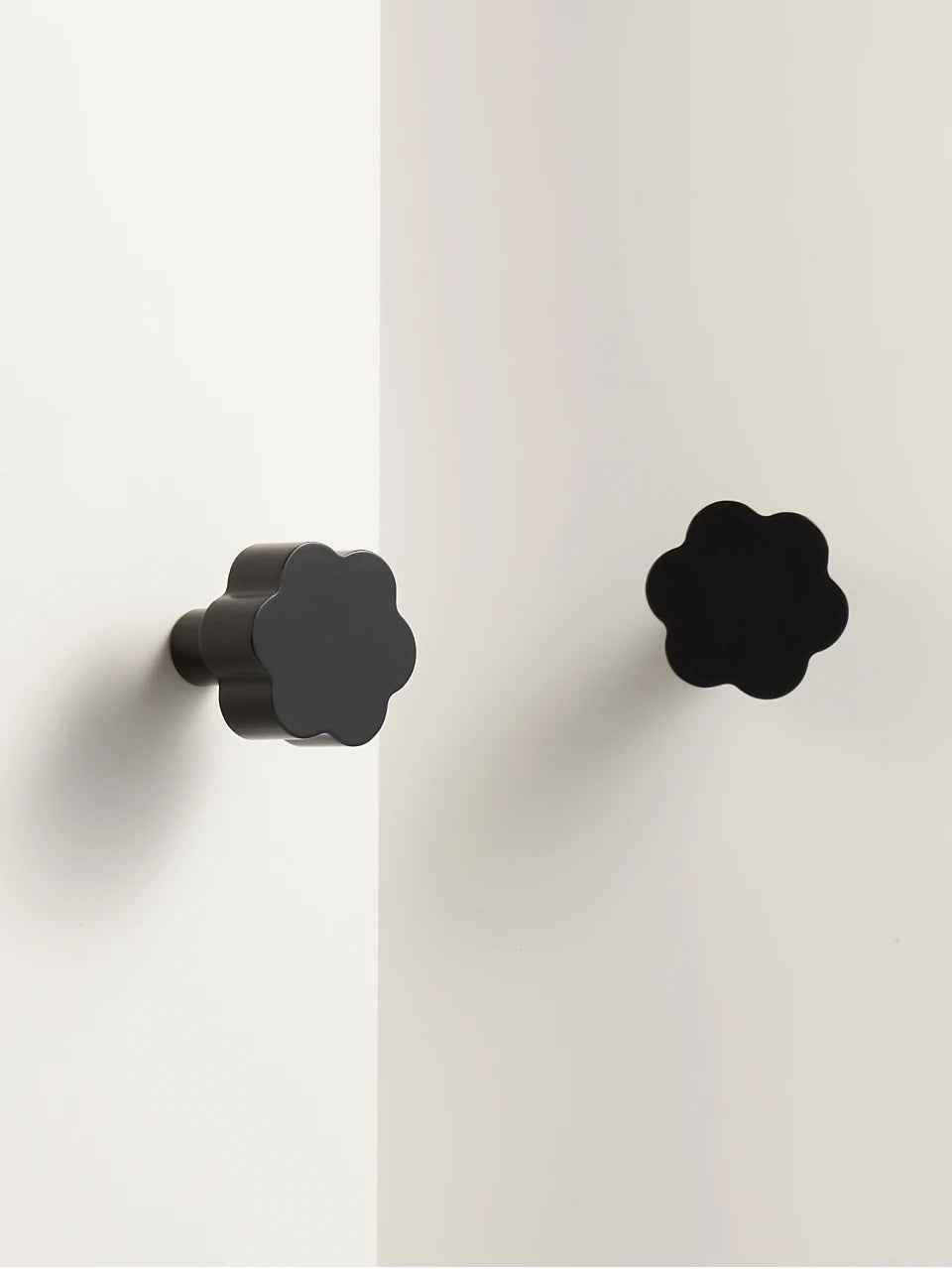 Two black flower cabinet knobs on a white door.