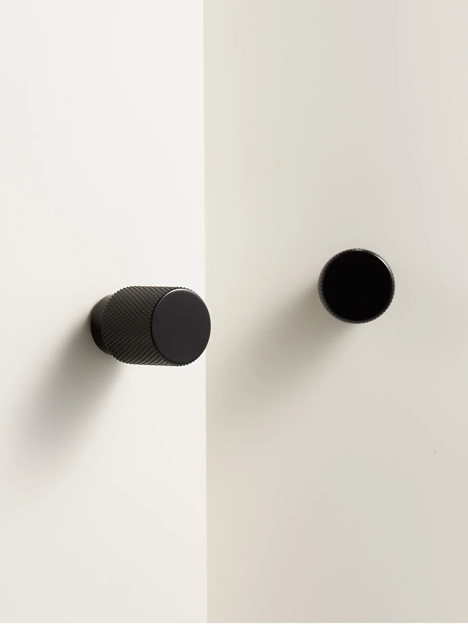 Two black knurled brass knobs on a white wall.
