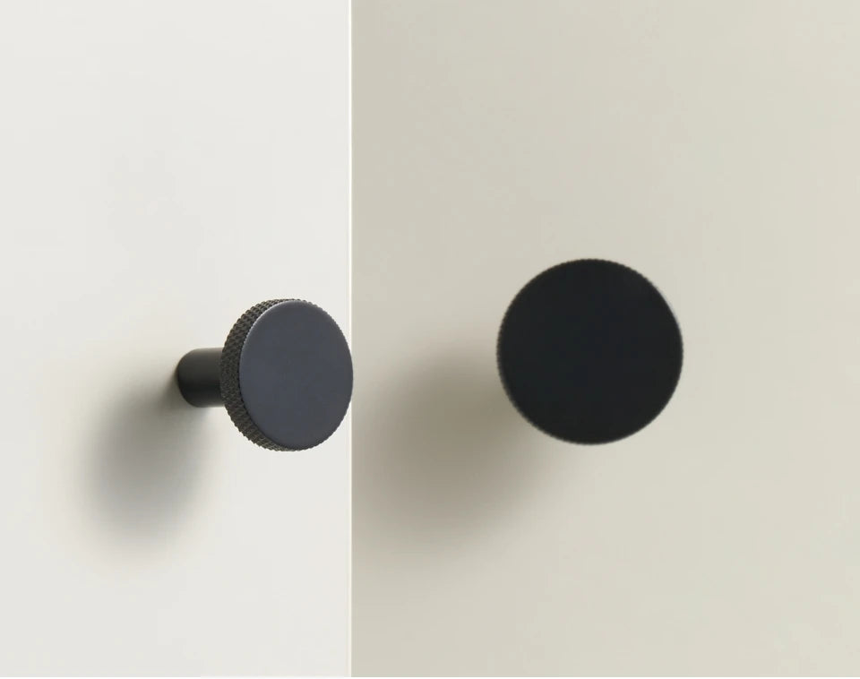 Two black matte antique cabinet knobs on a light grey background.