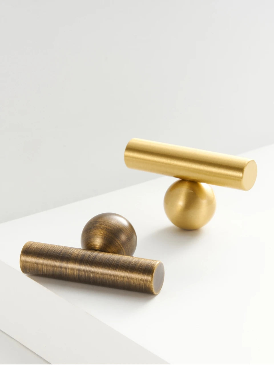 Two gold and antique brass round ball t-bars on a white surface.