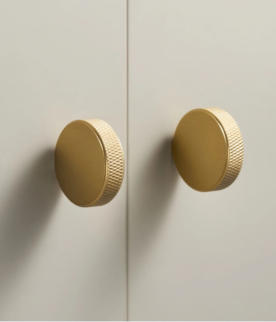 Two gold anti-slip cabinet knobs on a light grey door.