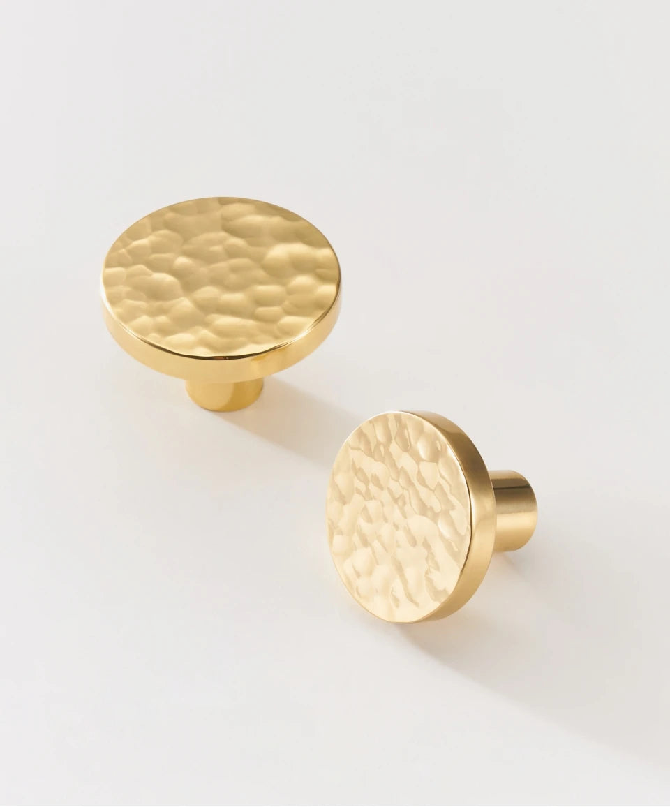 Two gold brass round hammered knobs on a light beige background.