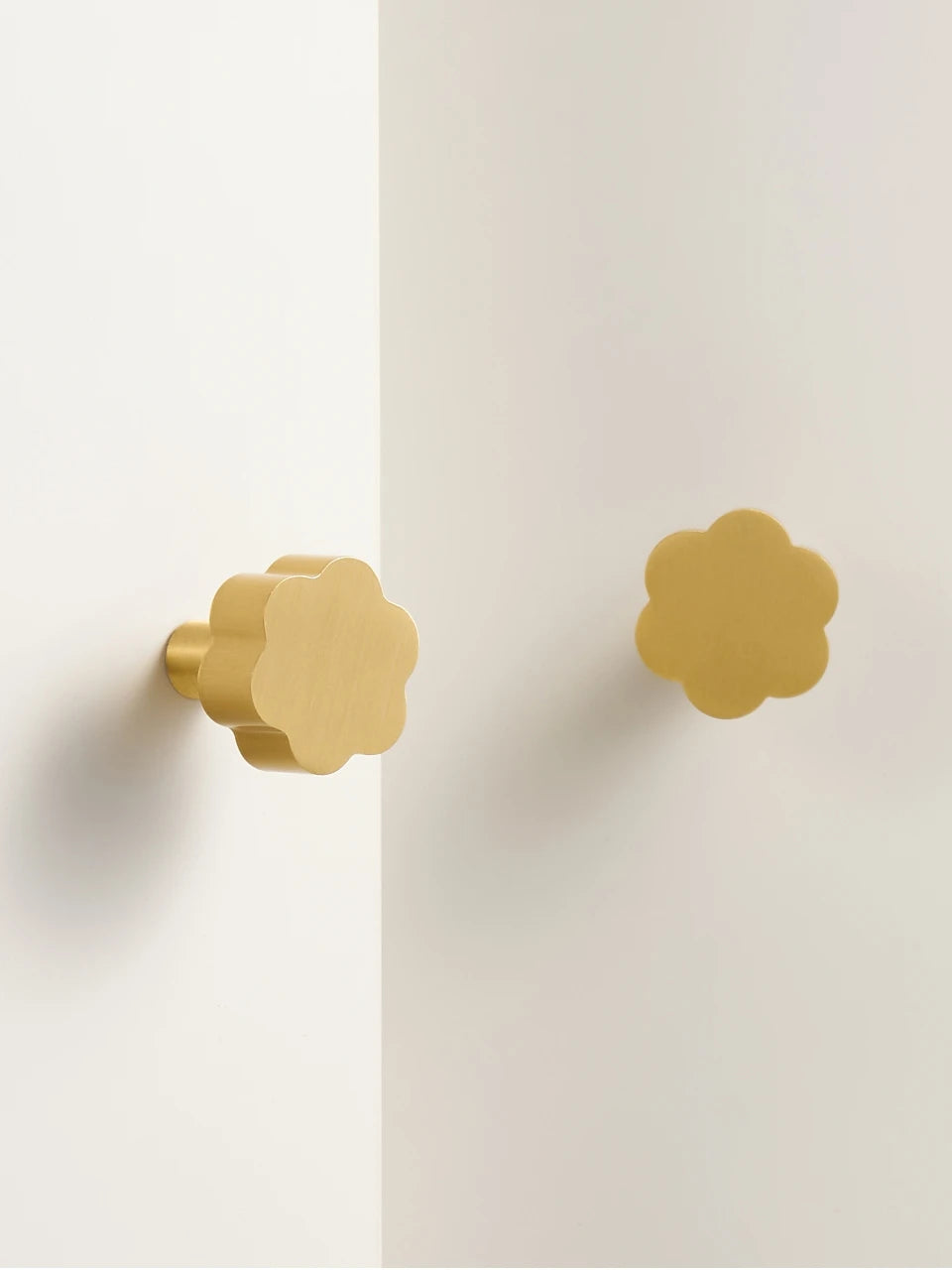 Two gold flower cabinet knobs on a white door.