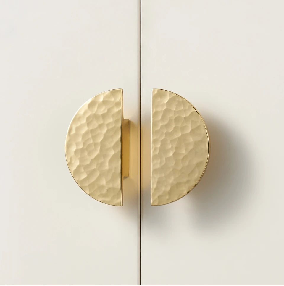 Two gold half circle cabinet knobs on a white door.