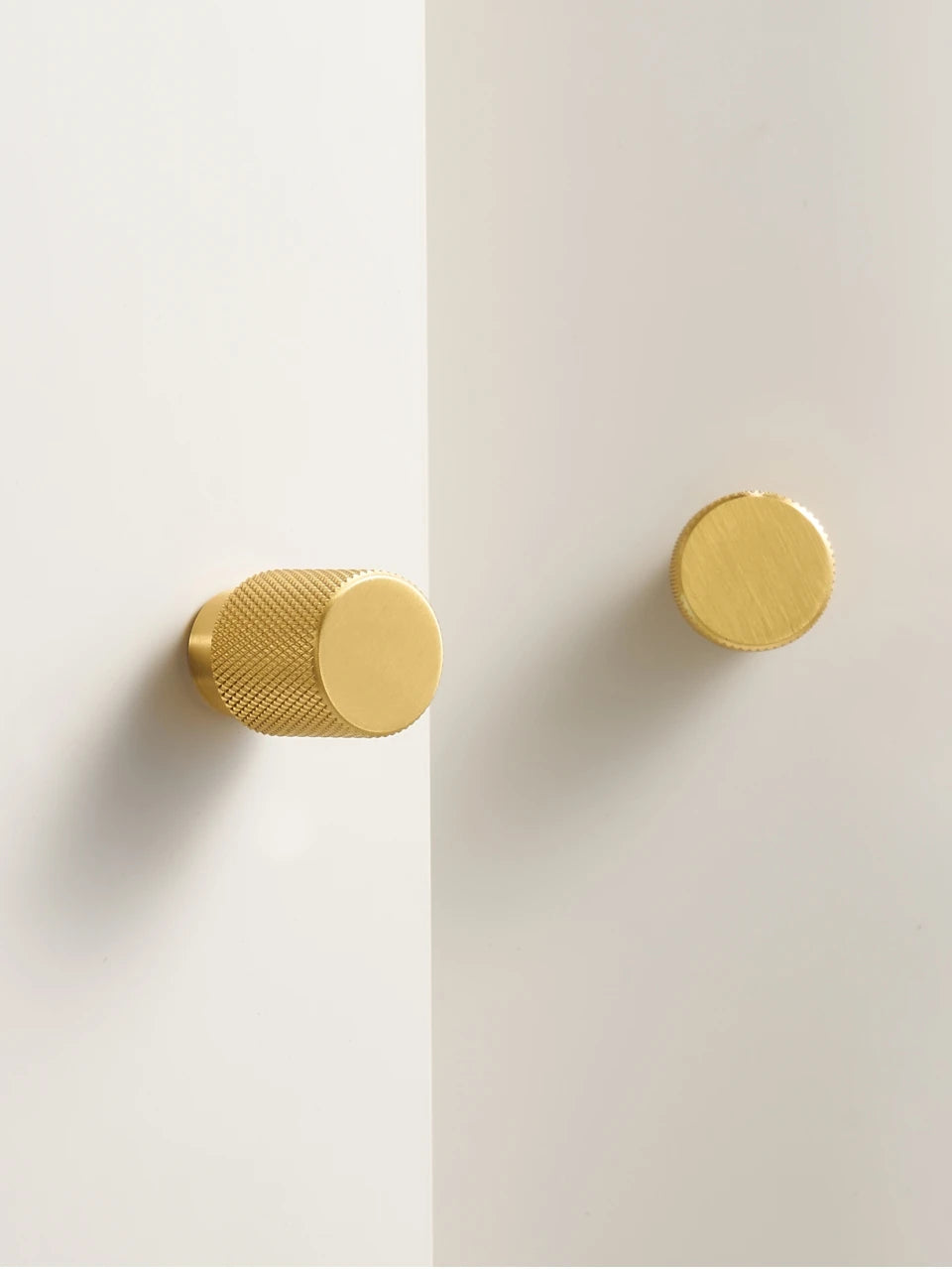 Two gold knurled brass knobs on a white wall.