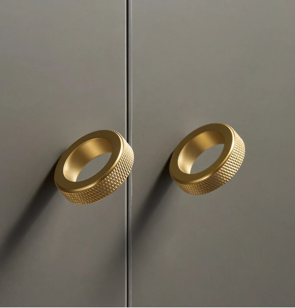 Three gold knurled ring cabinet knobs on a light beige background.