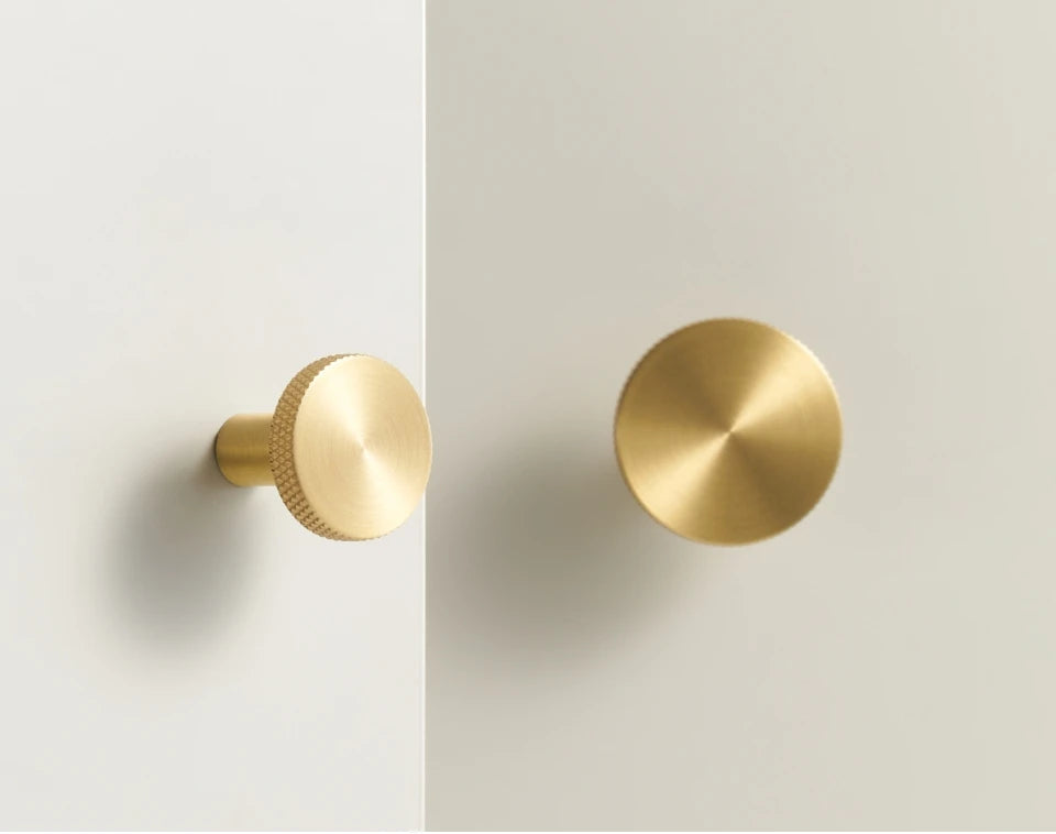 Two gold matte antique cabinet knobs on a light grey background.