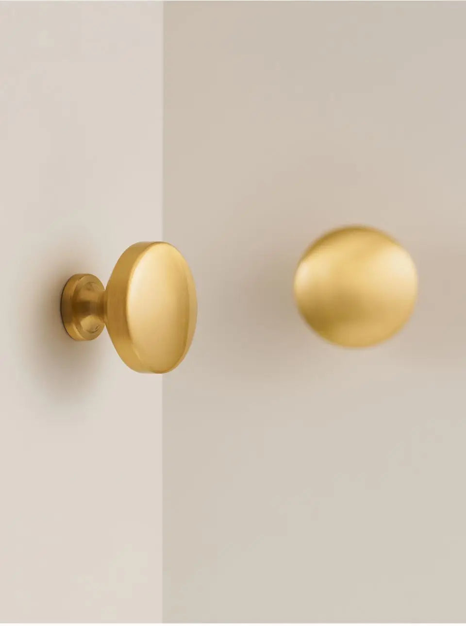 Two gold solid brass door knobs on a beige door.