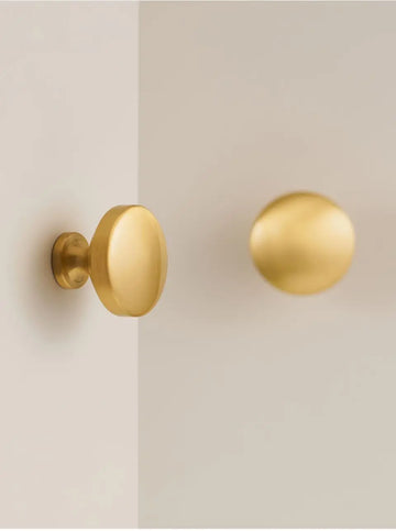 Two gold solid brass door knobs on a beige door.