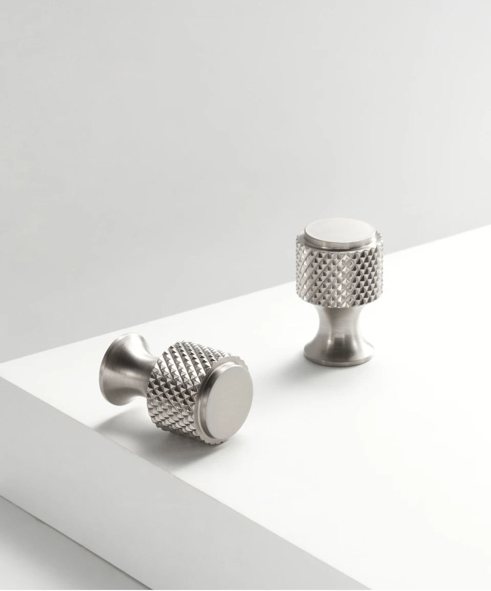 Two knurled brass nickel cabinet knobs on white shelf.