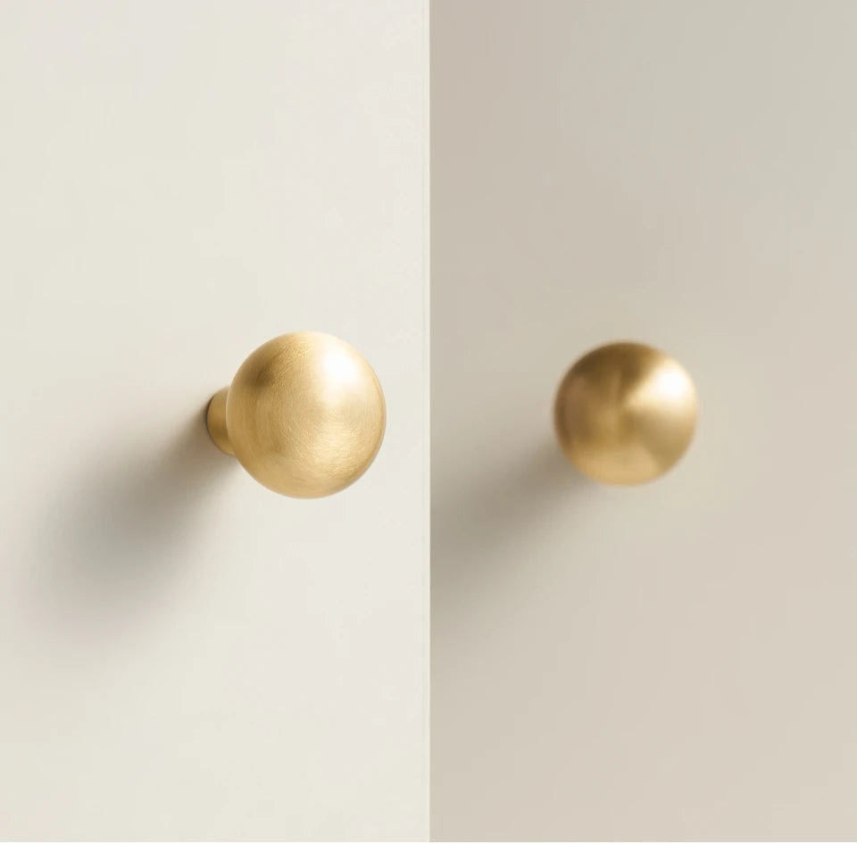 Two solid brass smooth gold cabinet round knobs on a light beige background.