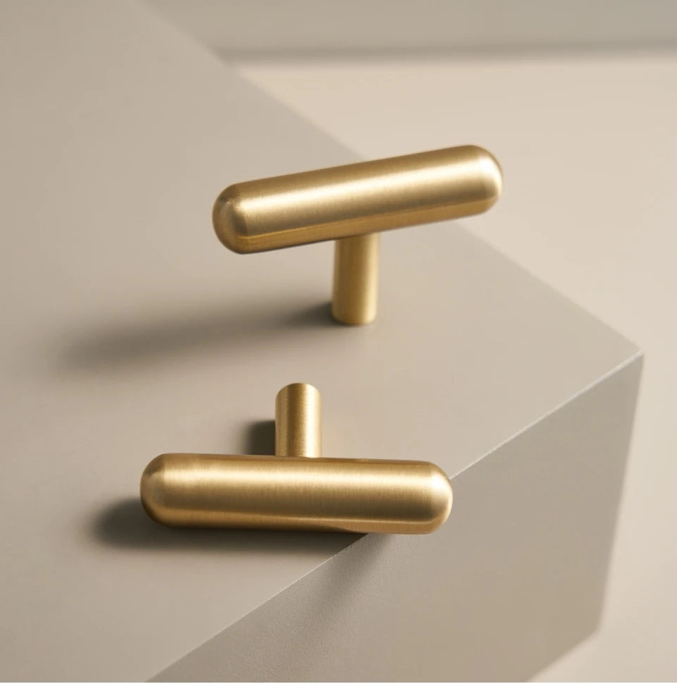 Two solid brass smooth gold cabinet round t-bars on a light beige background.