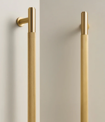 Two solid gold brass linear handles on a neutral background.