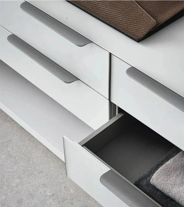 Close-up of a white dresser with grey edge pulls and an open drawer, showing a grey interior.
