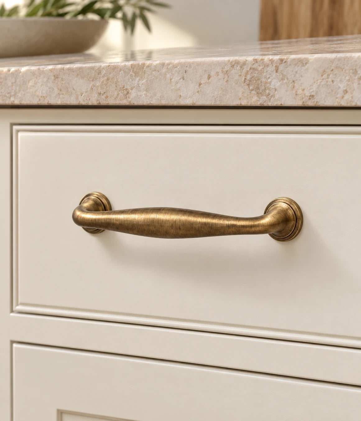 Antique brass arched cabinet pull installed on a cream drawer